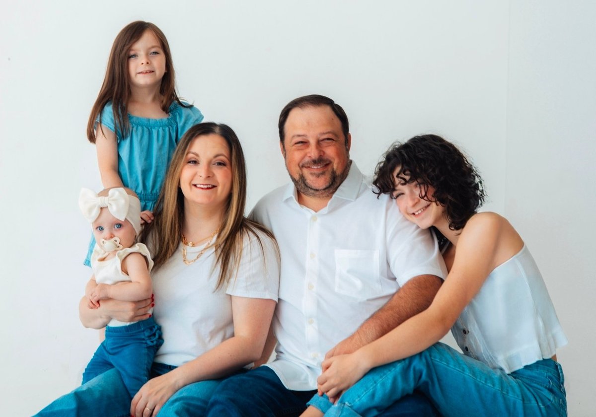 Family portrait of four people smiling at camera against white background, wearing casual white and blue clothing